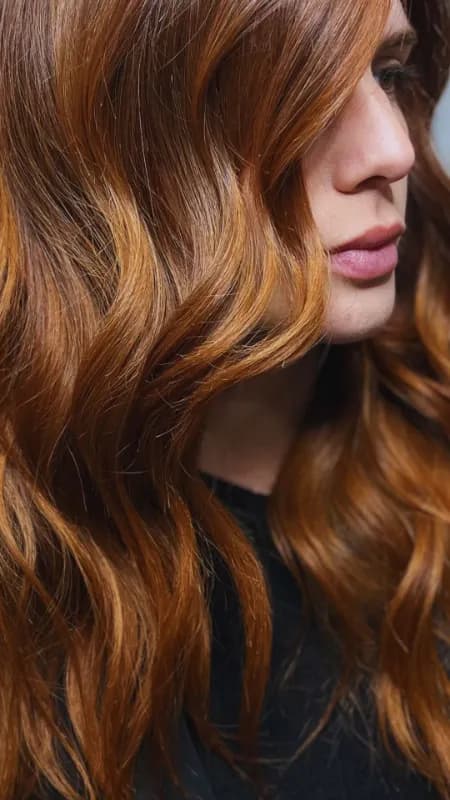 Primer plano del perfil de una mujer con el cabello largo y ondulado en tonos cobrizos, con brillo natural
