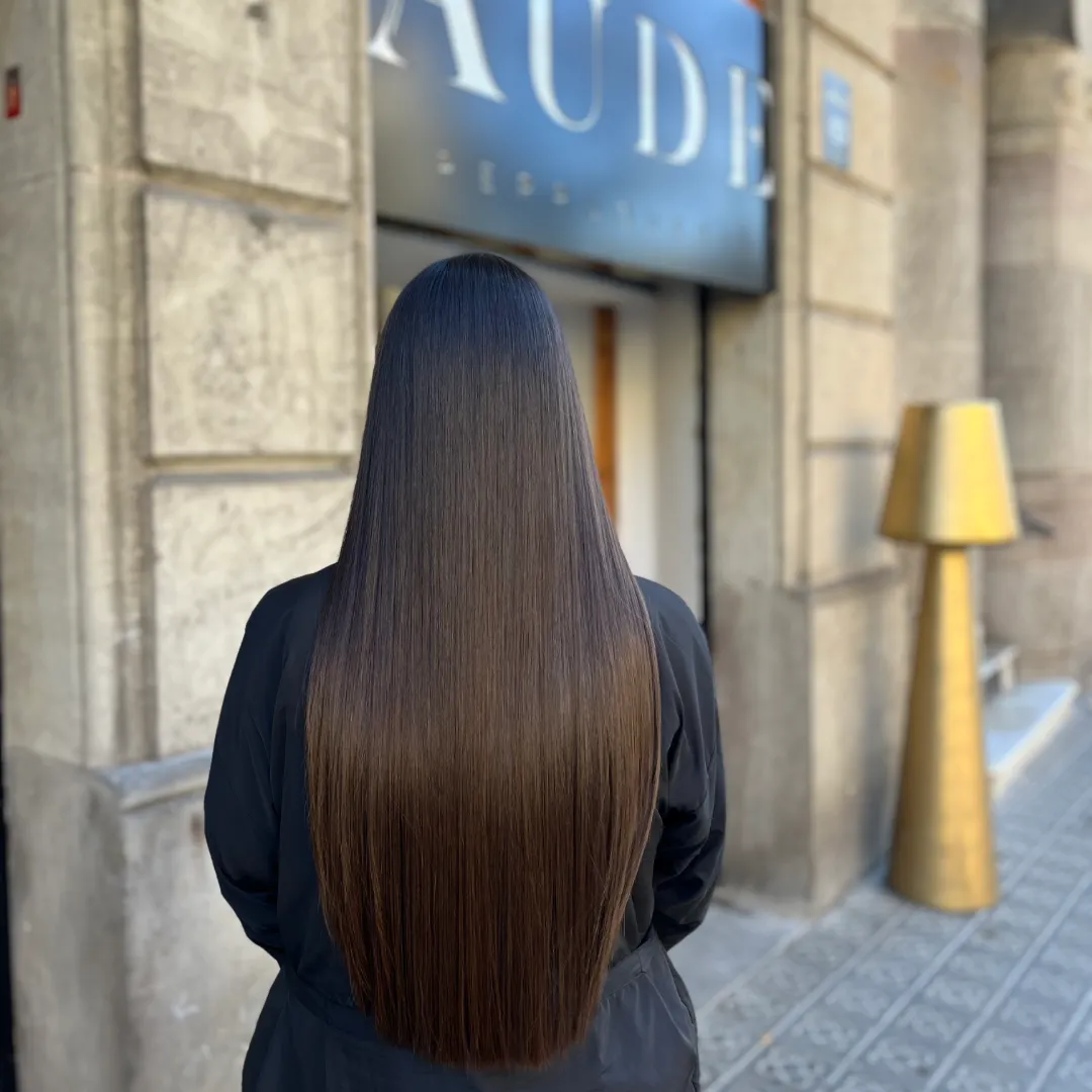 Back view of long, straight brown hair in front of the Aude salon storefront