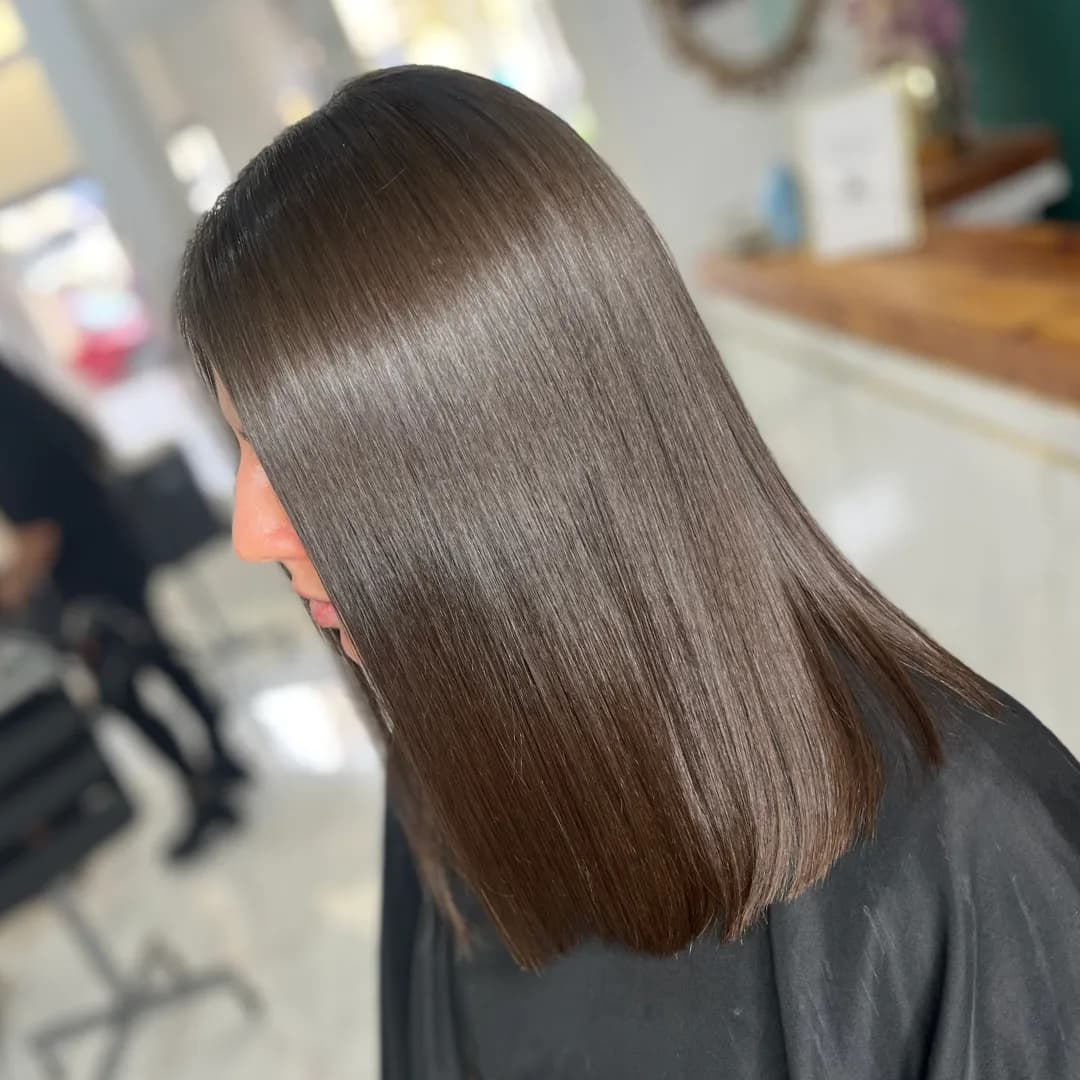 Straight, glossy shoulder-length brown hair seen in profile with a black salon cape