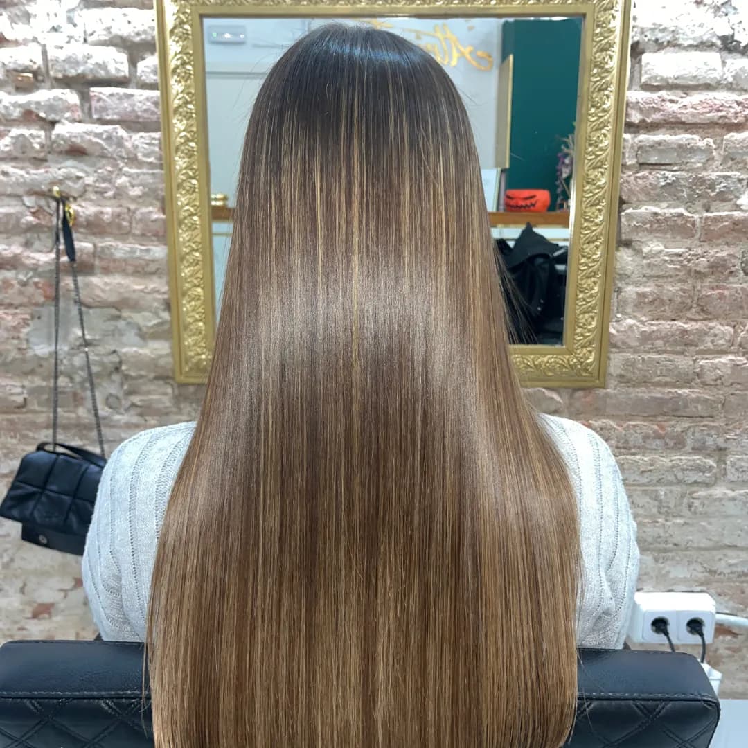 Back view of long, straight brown hair against a gold mirror and exposed brick wall