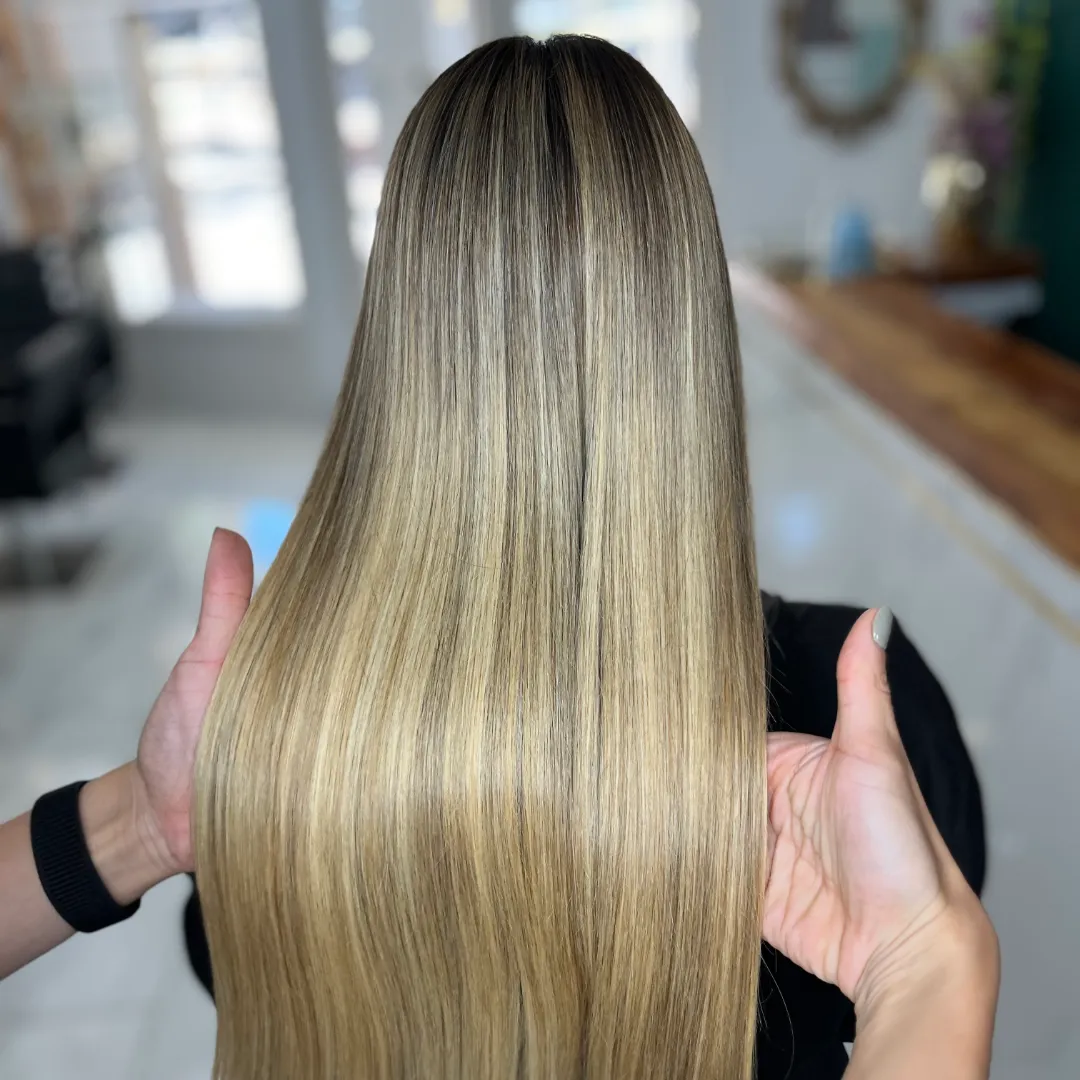 Hairstylist's hands holding long, straight blonde hair with dark roots