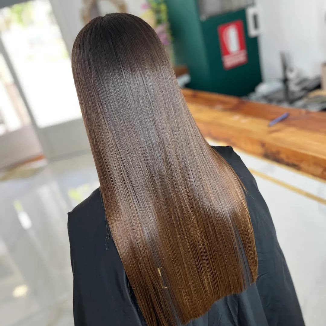 Back view of long, straight brown hair with a mirror-like finish over a black cape