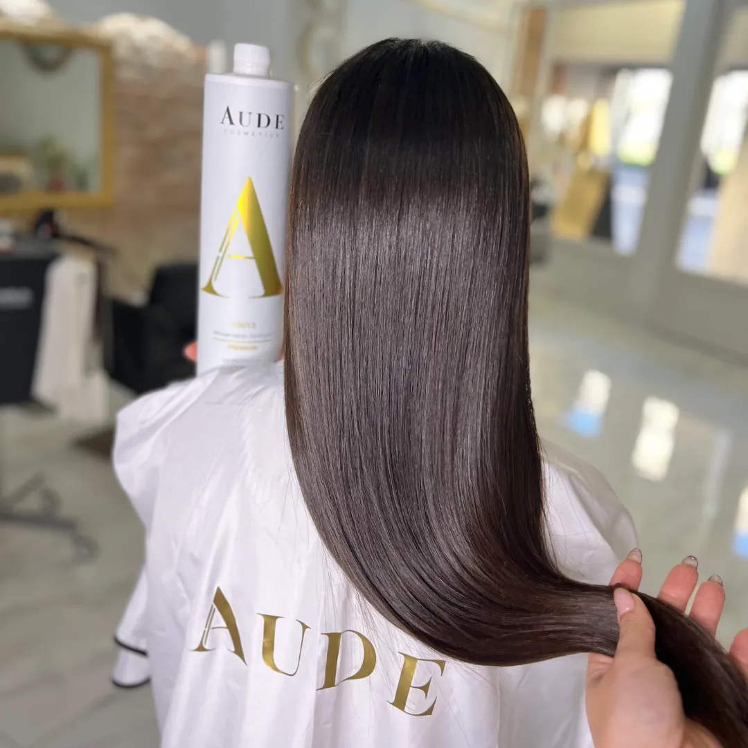 Hairstylist holding straight brown hair next to the Aude Cosmetics Synergic Alignment bottle